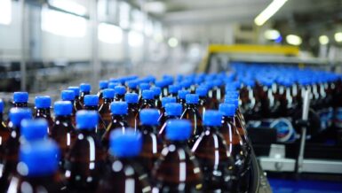 Amber PET soft drink bottles with blue caps moving along a beverage production line