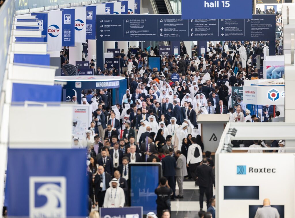 Visitors filling the main exhibition concourse at ADIPEC in Abu Dhabi, with signage to the halls and conference areas