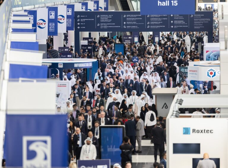 Visitors filling the main exhibition concourse at ADIPEC in Abu Dhabi, with signage to the halls and conference areas