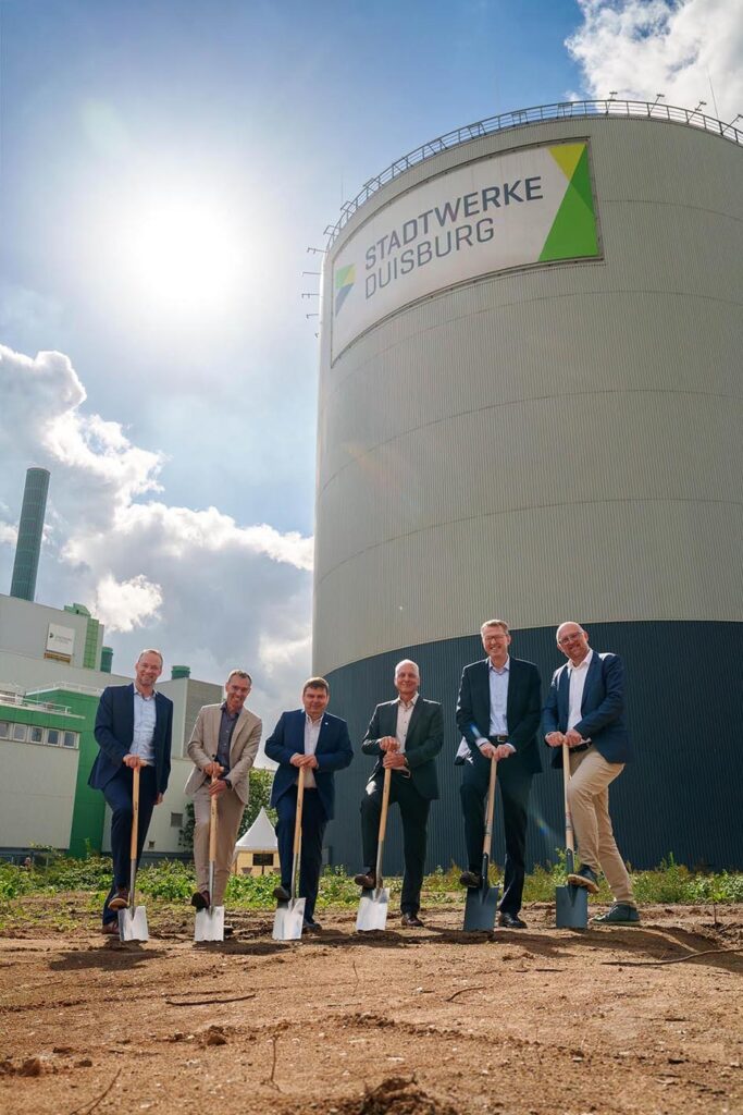 Six men holding spades at the ground-breaking ceremony in front of the Stadtwerke Duisburg heat storage tank at the Wanheim Energy Park