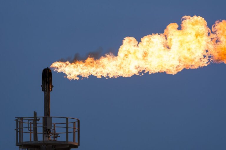Flare stack burning surplus gas against a blue sky