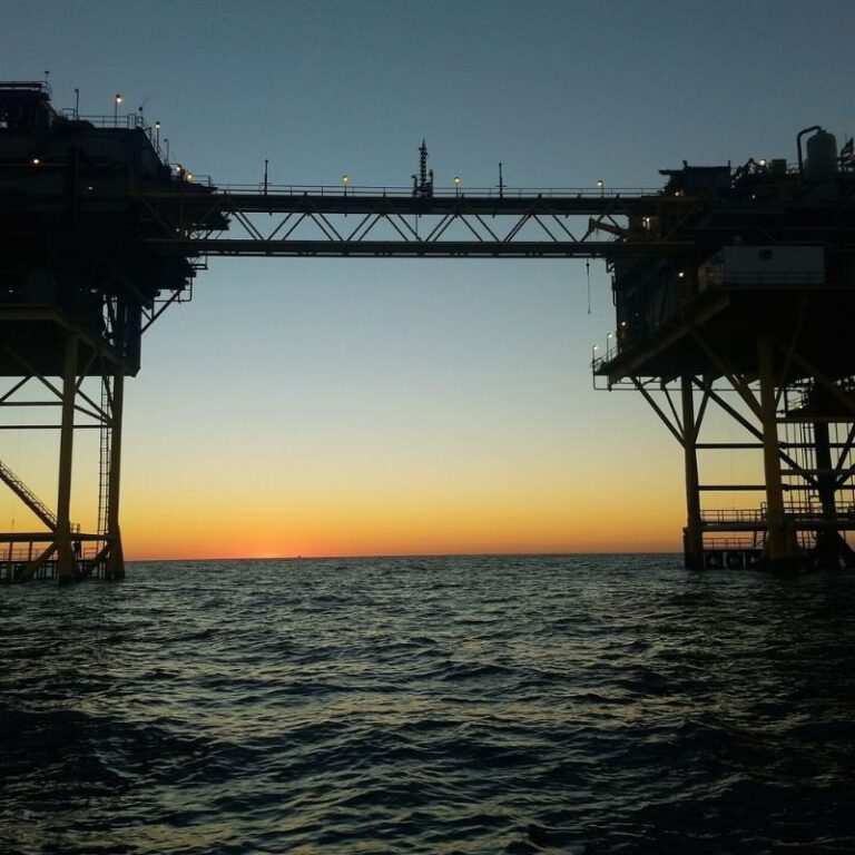 Offshore oil and gas platforms linked by a bridge at sunset, where high-pressure fluid power systems keep operations running