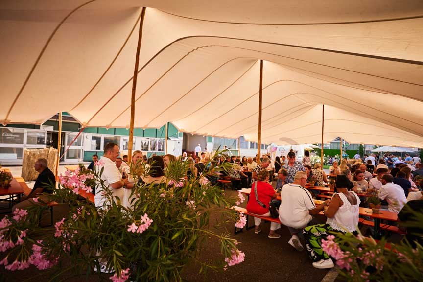 Guests seated at long tables in a large festival tent decorated with flowers