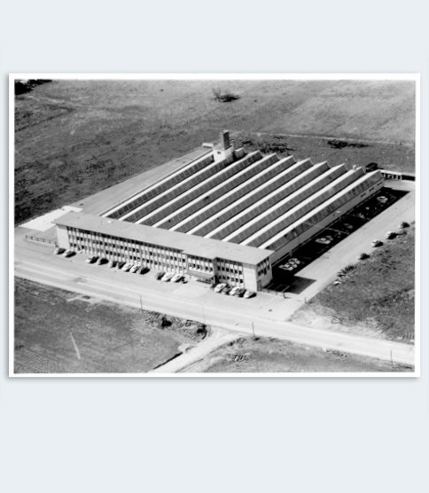 Aerial black-and-white photo of a large factory building with a sawtooth roof