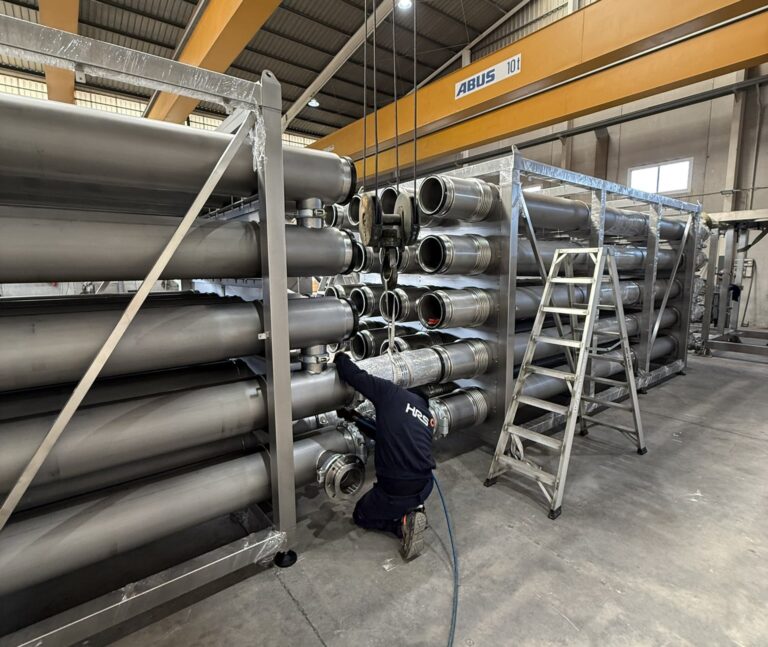 Technician assembling an HRS DTI Series heat exchanger array with stainless steel tubes in the factory