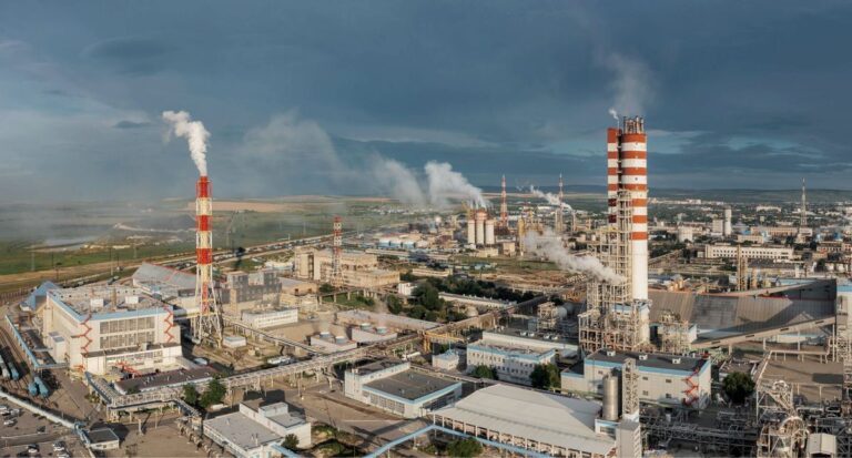 Aerial view of an industrial site with tall red and white stacks emitting steam