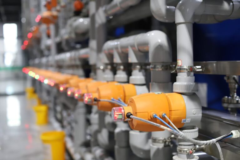 Row of inline process sensors with orange housings mounted on plant piping