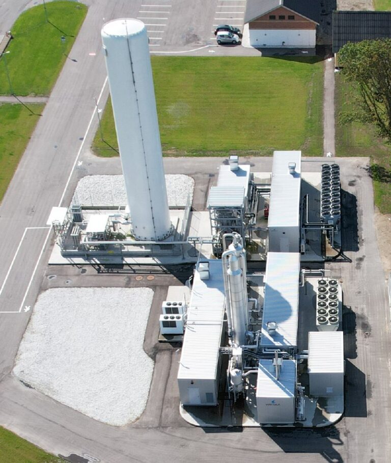 Aerial view of a biogas liquefaction plant with a tall vertical LNG storage tank and process modules