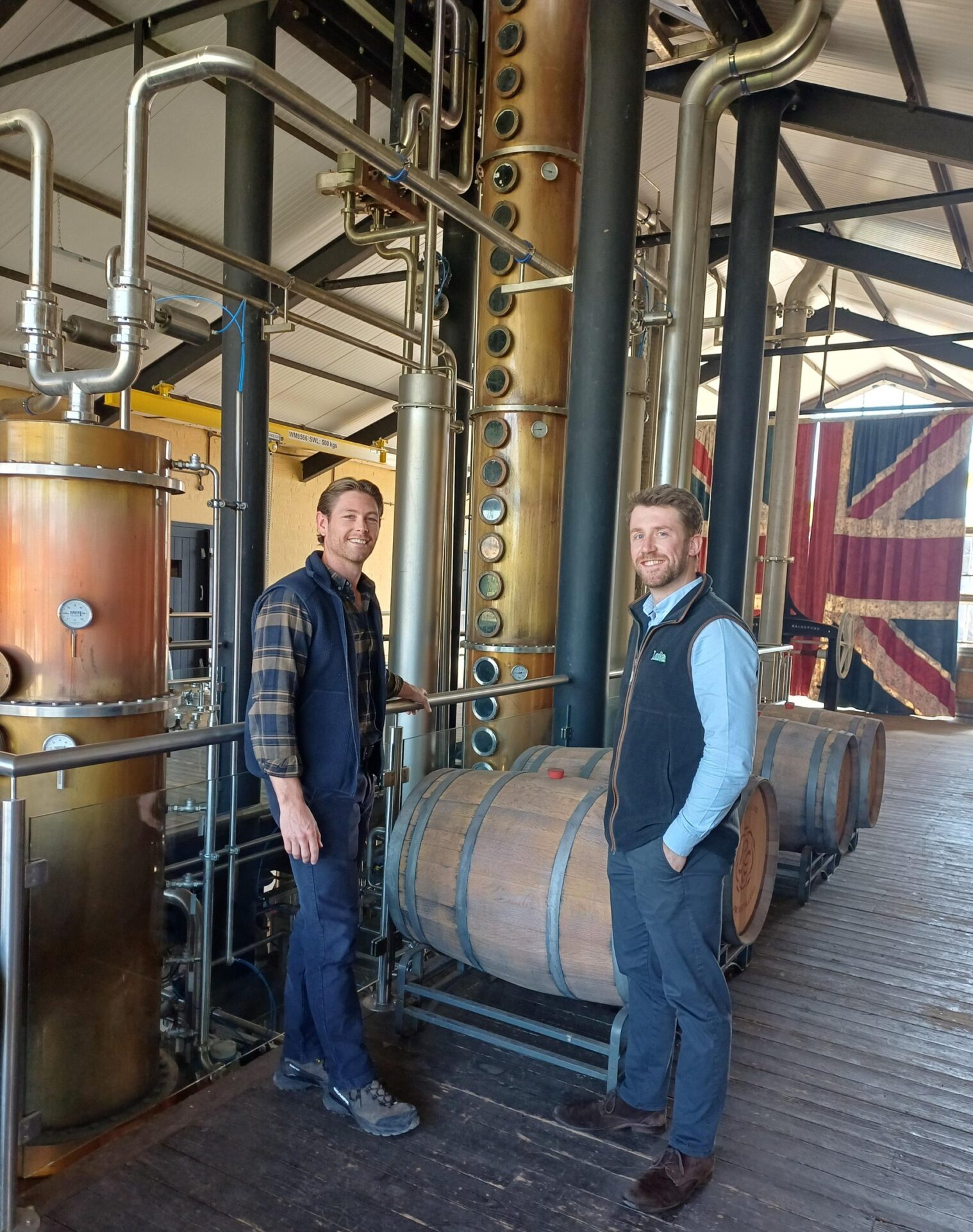 Two men standing beside the copper column still and oak casks at Rosemaund Farm Distillery near Hereford
