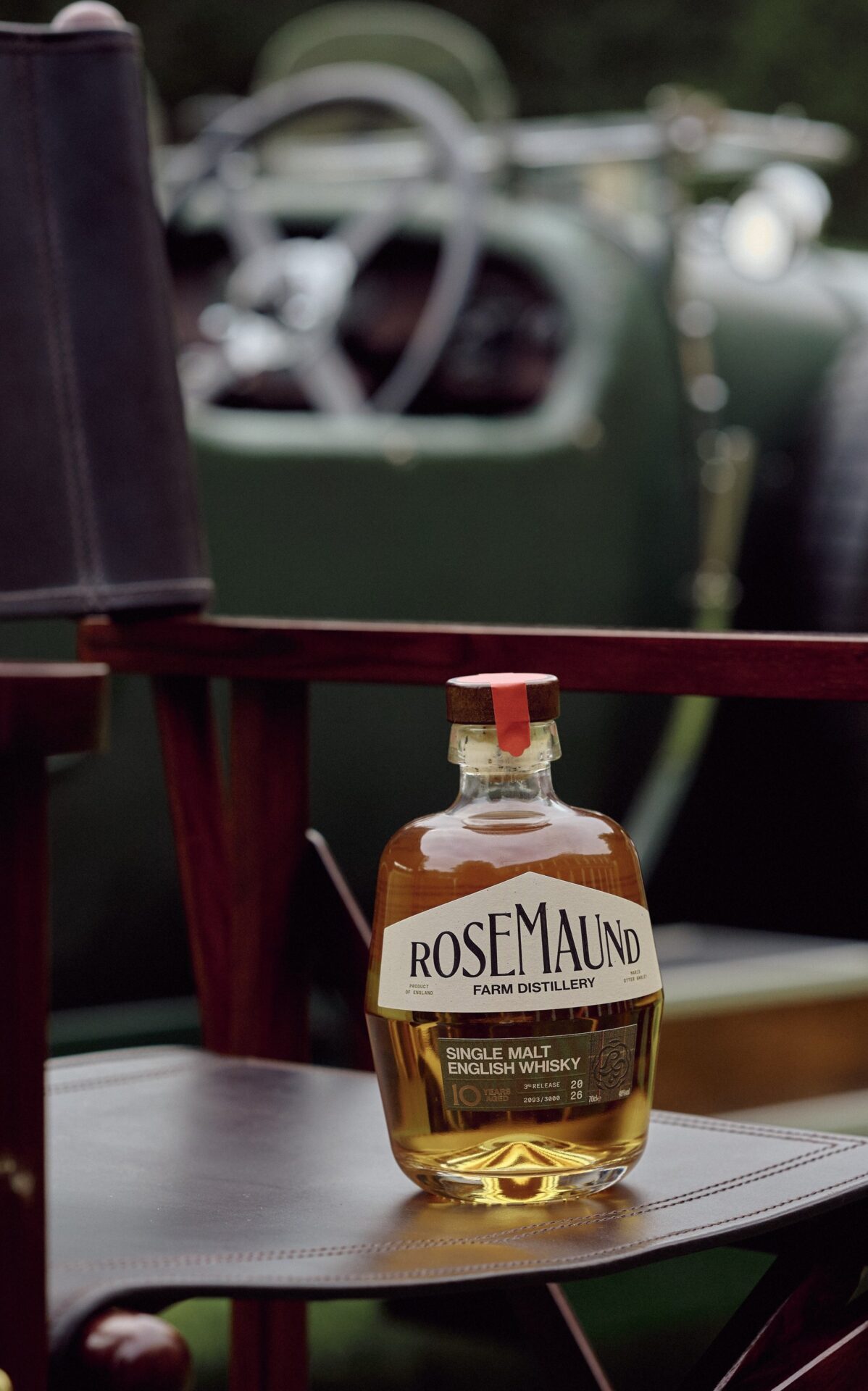 Bottle of Rosemaund single malt English whisky on a leather folding chair with a vintage car in the background