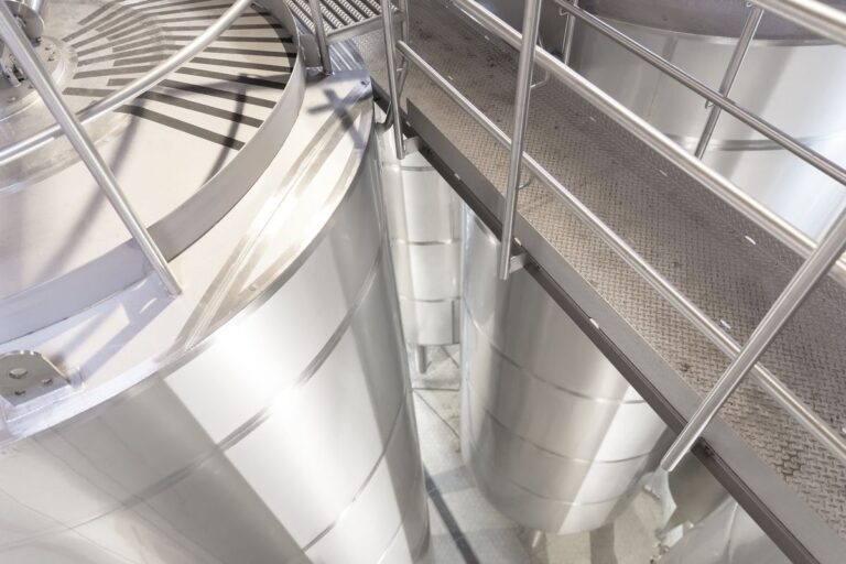 Row of stainless steel storage silos seen from a walkway