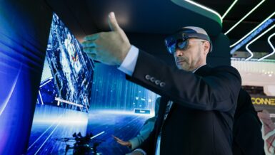 Visitor wearing a mixed-reality headset gestures at a large screen during a technology demonstration at ADIPEC in Abu Dhabi