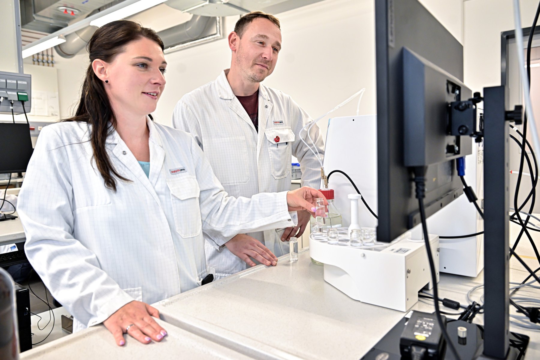 Two Analytik Jena employees in lab coats working with an analytical instrument in the Ilmenau laboratory