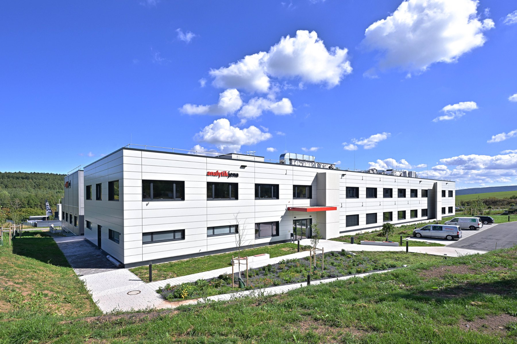 Two-storey white Analytik Jena building in Ilmenau surrounded by greenery and hills