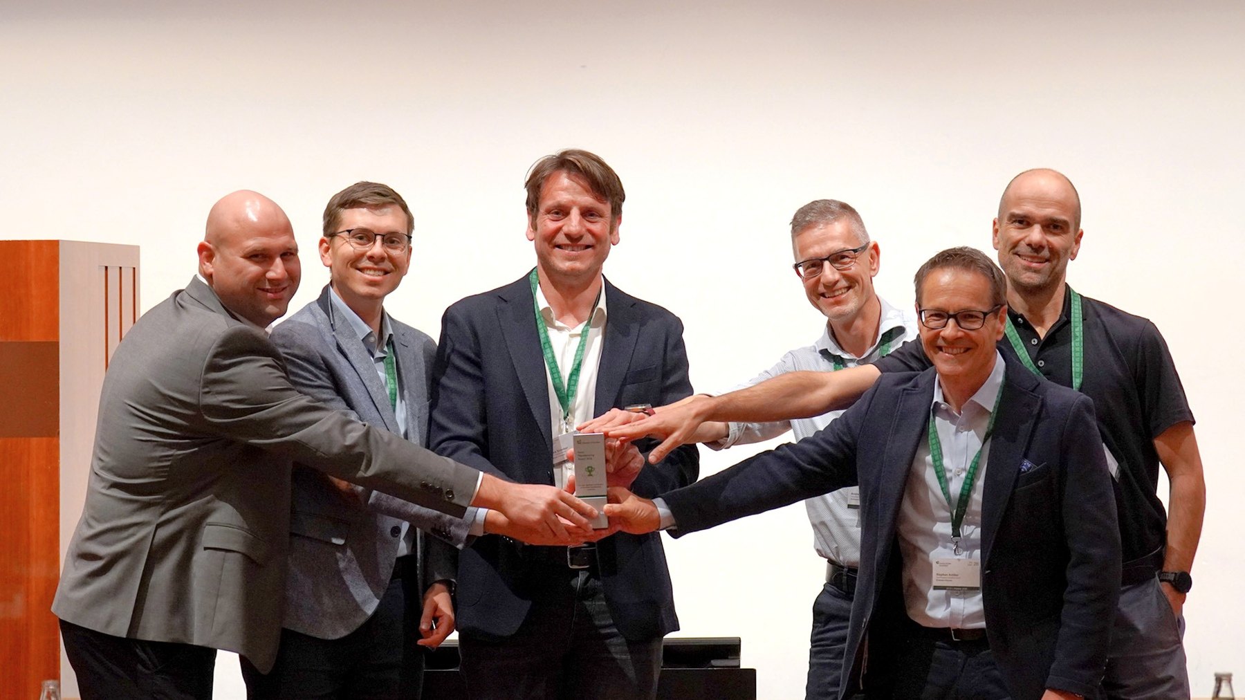 Six men in suits jointly holding the Swiss Manufacturing Award trophy on stage at the St. Gallen Production Management Conference