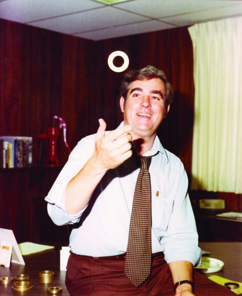 Man in a 1970s office flipping a seal ring, with bearing isolators on the desk