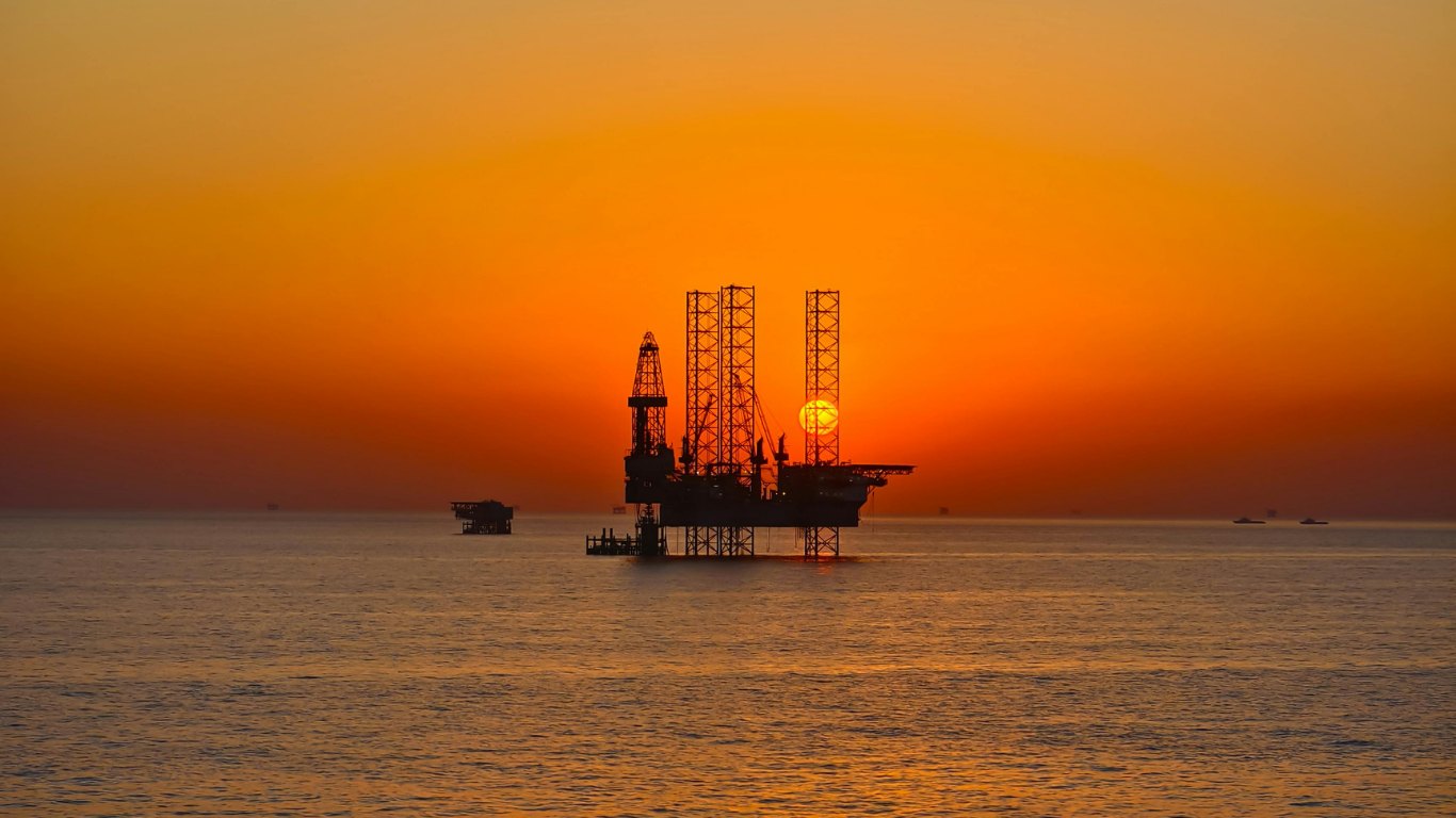 Offshore jack-up drilling platform silhouetted against an orange sunset