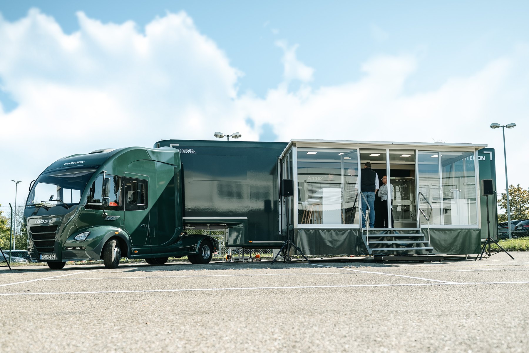 The Syntegon Annex 1 Roadshow truck with its glass-walled exhibition trailer and visitors inside, parked at the Crailsheim site