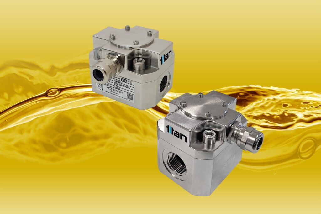 Two stainless steel Titan Enterprises Oval Gear (OG) flowmeters for liquid flow measurement against a golden liquid background